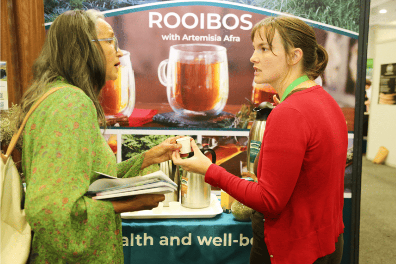 An exhibitor hands a Rooibos tea sample to an international buyer at The Good Life Show Africa B2B matchmaking event.